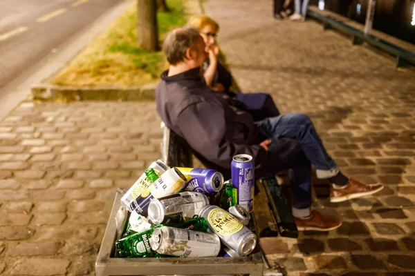 Poubelle débordant de canettes et bouteilles vides sur un trottoir parisien, symbole des soirées sans alcool.