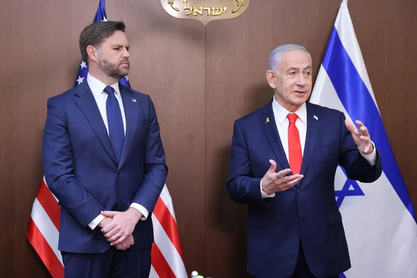 Benjamin Netanyahu s'adressant à un interlocuteur lors d'une rencontre avec des responsables américains, drapeaux des deux pays en arrière-plan.