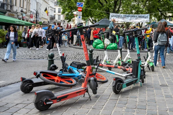 Trottinettes en libre-service garées en désordre sur une rue pavée à Bruxelles.