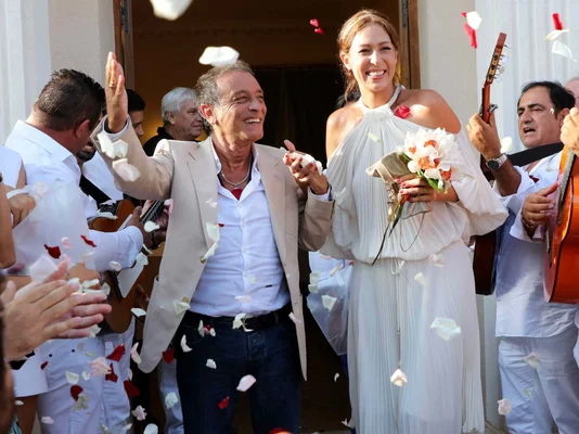Félix Gray et son épouse le jour de leur mariage, accueillis par des musiciens et une pluie de pétales.