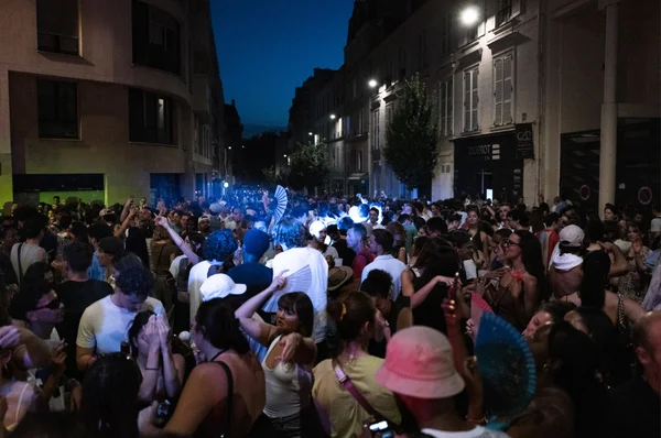 Foule dense dans une rue étroite lors de la Fête de la musique, avec des éventails pour se rafraîchir.