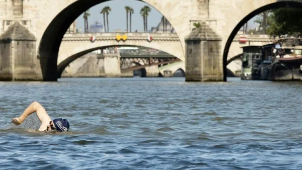 Nageur en crawl dans la Seine, avec arches de pont et palmiers en toile de fond.