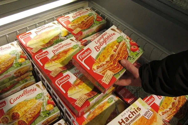 Une main choisit une boîte de lasagnes bolognaise Findus parmi d'autres plats surgelés dans un rayon de supermarché.