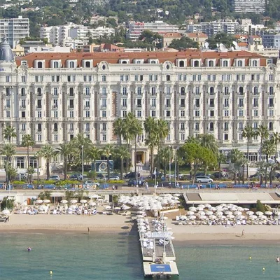 L'hôtel InterContinental Carlton Cannes, façade majestueuse et plage avec parasols.