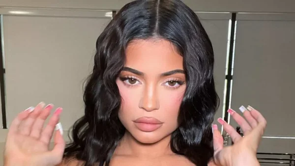 Portrait rapproché de Kylie Jenner, mains levées, mettant en valeur son maquillage et ses ongles.