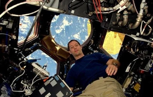 Astronaute en apesanteur dans le module Cupola de l'ISS, avec vue sur la Terre.
