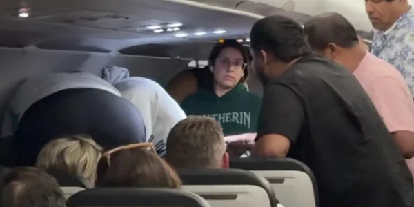 Passagers debout dans l'allée lors de l'incident, dont une femme en sweat 'Slytherin'.