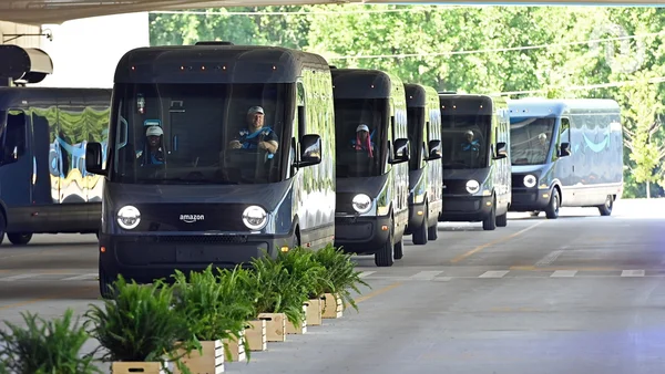 Flotte de fourgons électriques Amazon alignés dans un centre de distribution, conducteurs visibles à bord.