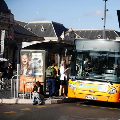 Un bus jaune du réseau Lignes d'Azur à un arrêt, avec des passagers en attente, devant un bâtiment SNCF à Nice.