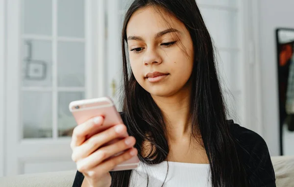 Une jeune femme utilise son smartphone rose dans un intérieur flou.
