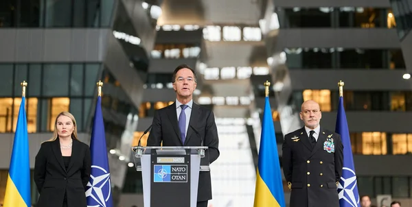 Conférence de presse de l'OTAN en soutien à l'Ukraine, avec les drapeaux alliés en arrière-plan.