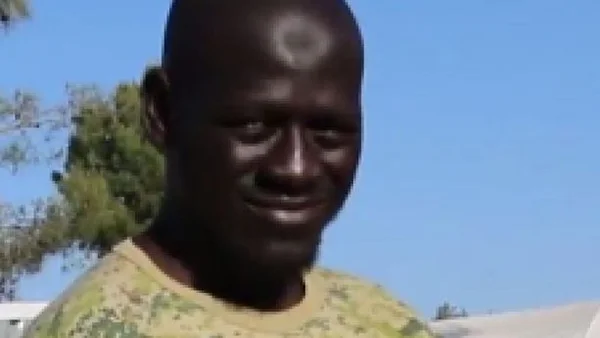 Un homme souriant, vêtu d'un t-shirt camouflage, photographié en extérieur.