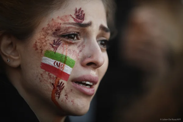 Une manifestante iranienne avec le drapeau iranien peint sur la joue et des marques rouges sur le visage.