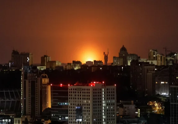 Vue de Kiev la nuit avec une lueur d'incendie à l'horizon, illustrant l'attaque russe en cours.