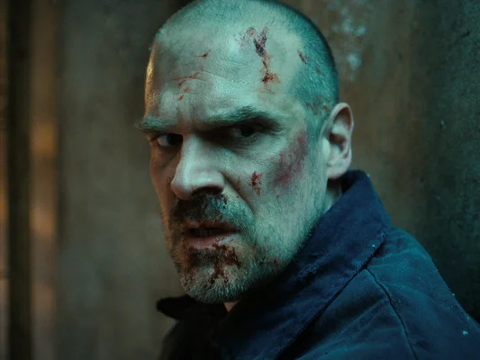 David Harbour, le visage ensanglanté et crasseux, dans une scène intense.