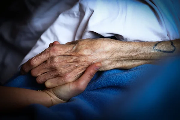 Main jeune tenant la main d'une personne âgée sur une couverture bleue.