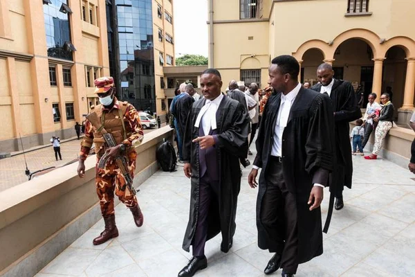 Des avocats escortés par un soldat dans un couloir du tribunal ougandais.