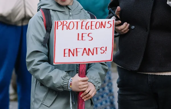 Manifestante tenant une pancarte 'PROTÉGEONS LES ENFANTS !' lors d'un rassemblement.