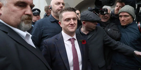 Tommy Robinson lors d'une apparition publique, entouré de médias et de sécurité.