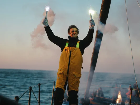 Charlie Dalin rendant hommage avec des fusées éclairantes sur son bateau, au coucher du soleil.