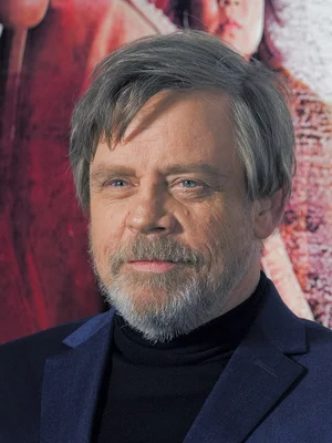 Portrait de Mark Hamill devant un fond d'affiche rouge.