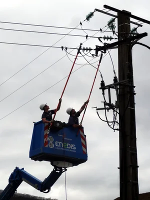Des techniciens d'Enedis effectuent des travaux sous tension sur une ligne HTA, illustrant les opérations de maintenance du réseau électrique.