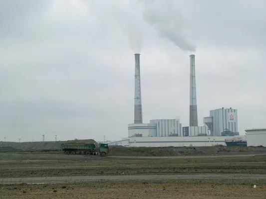 Vue d'une centrale électrique d'EDF avec des cheminées fumantes et un camion-benne au premier plan.