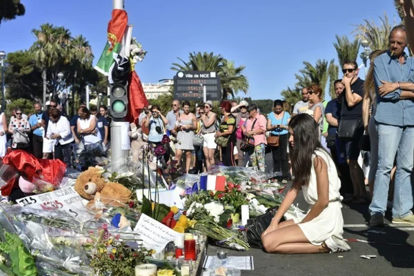 Une jeune fille assise près d'un mémorial de fleurs, bougies et peluches en hommage aux victimes de l'attentat du 14 juillet 2016 à Nice.
