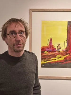 Brüno, dessinateur de la série Lucky Luke, posant à côté d'une illustration de l'univers du cow-boy solitaire.