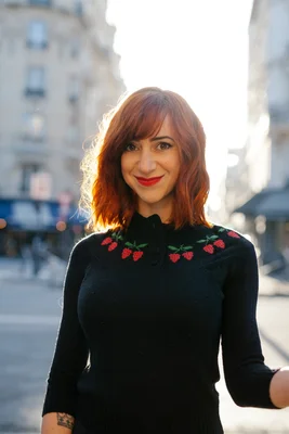 Pénélope Bagieu dans un cadre urbain, arborant un pull aux fraises.