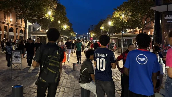 Jeunes supporters dans une rue piétonne à Toulouse, au crépuscule, avec un maillot de l'équipe de France.