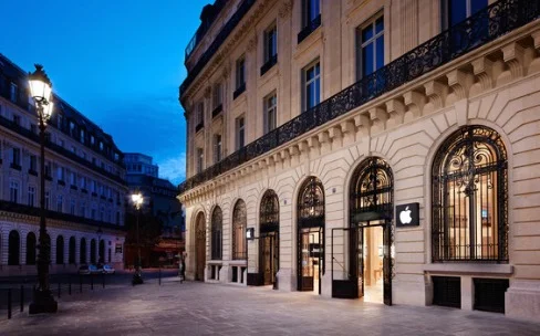 Apple Store parisien dans un immeuble haussmannien illuminé en soirée.