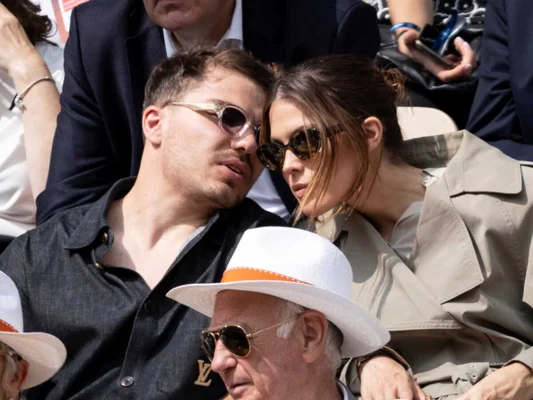 Antoine Dupont et Iris Mittenaere en extérieur, partageant un moment tendre, avec un spectateur au premier plan.