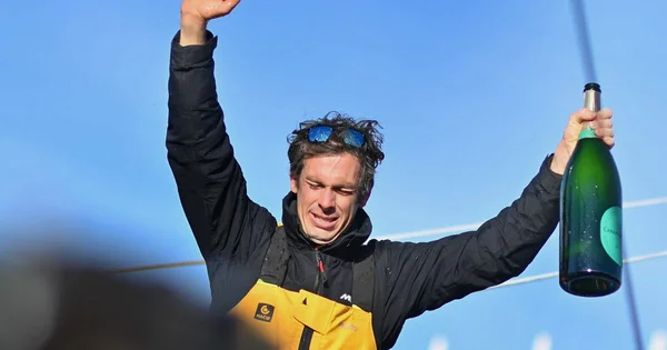 Charlie Dalin célèbre sa victoire au Vendée Globe en brandissant une bouteille de champagne.