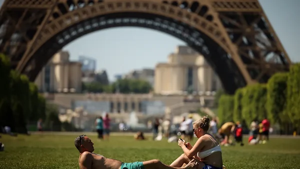 Paris : des promeneurs profitent du Champ-de-Mars sous un soleil de plomb, avec la Tour Eiffel en toile de fond.