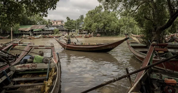 Vue d'une rivière birmane avec des bateaux à moteur et des habitations sur pilotis.