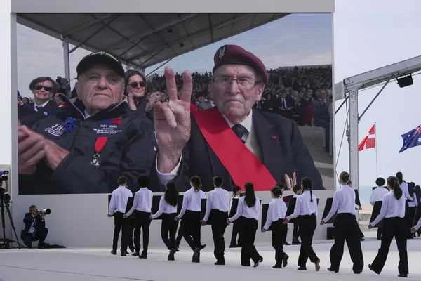 Hommage aux vétérans du Débarquement lors d'une cérémonie commémorative, avec des jeunes performers sur scène.