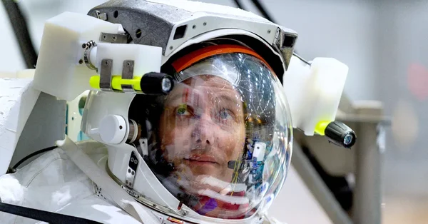 Gros plan sur un astronaute en casque spatial, visière ouverte, révélant son visage.