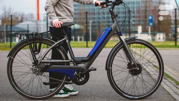 Un cycliste et son vélo électrique bleu et noir sur un chemin pavé en milieu urbain.