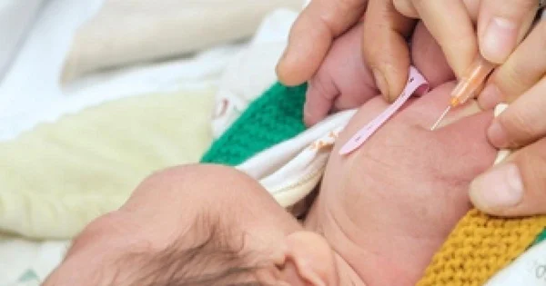 Injection de vitamine K administrée dans la main d'un nouveau-né par un professionnel de santé.