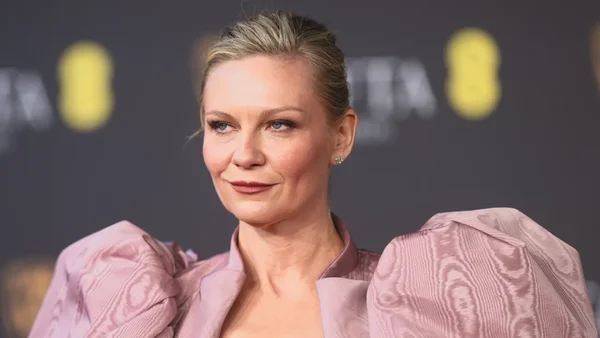 Kirsten Dunst en robe rose à manches bouffantes lors d'un événement, cheveux blonds relevés
