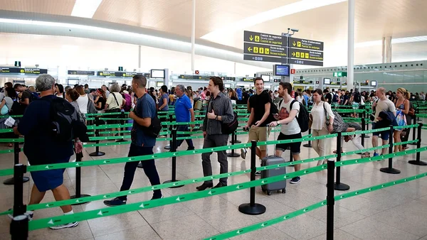 Foule de voyageurs attendant dans une zone de sécurité aéroportuaire très fréquentée, avec des barrières et panneaux de signalisation, en lien avec les perturbations du nouveau système EES.