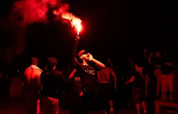 Personne brandissant un fumigène rouge lors d'un rassemblement nocturne, évoquant l'ambiance des matchs à risque de la Coupe du monde 2026.