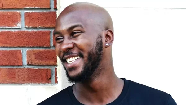 O'Shae Sibley, souriant, photographié devant un mur de briques.