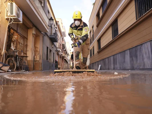 Secouriste nettoyant une rue inondée après des intempéries, illustrant les conséquences du changement climatique.