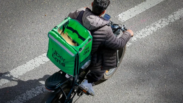 Un coursier à scooter avec un sac Uber Eats vert.