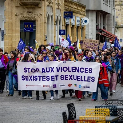 Manifestants défilant avec une banderole 'STOP AUX VIOLENCES SEXISTES ET SEXUELLES' dans une rue commerçante.
