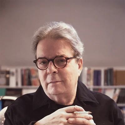 Douglas Kennedy, à la Maison de la poésie, devant une bibliothèque, un stylo à la main.