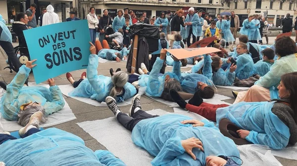 Manifestants en blouses médicales allongés au sol, brandissant une pancarte pour réclamer des soins palliatifs.