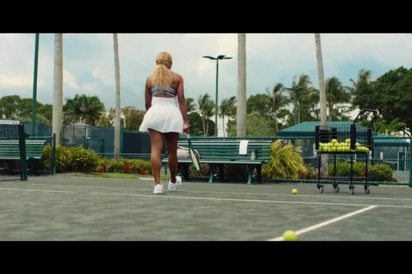 Joueuse de tennis s'éloignant sur un court dur, dans un décor estival.